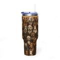 A tall insulated tumbler with a clear lid and straw, featuring an all-over print of various dog portraits on a dark brown patterned background.